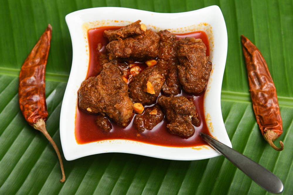 pickling beef - Kerala beef pickle in a white bowl on banana leaf with dried red chilies and spicy oil